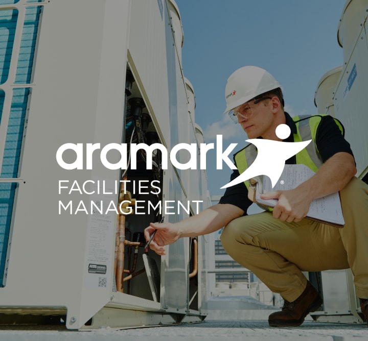 Man in hard hat and safety vest kneeling down with the Aramark Facilities Management logo overlayed.