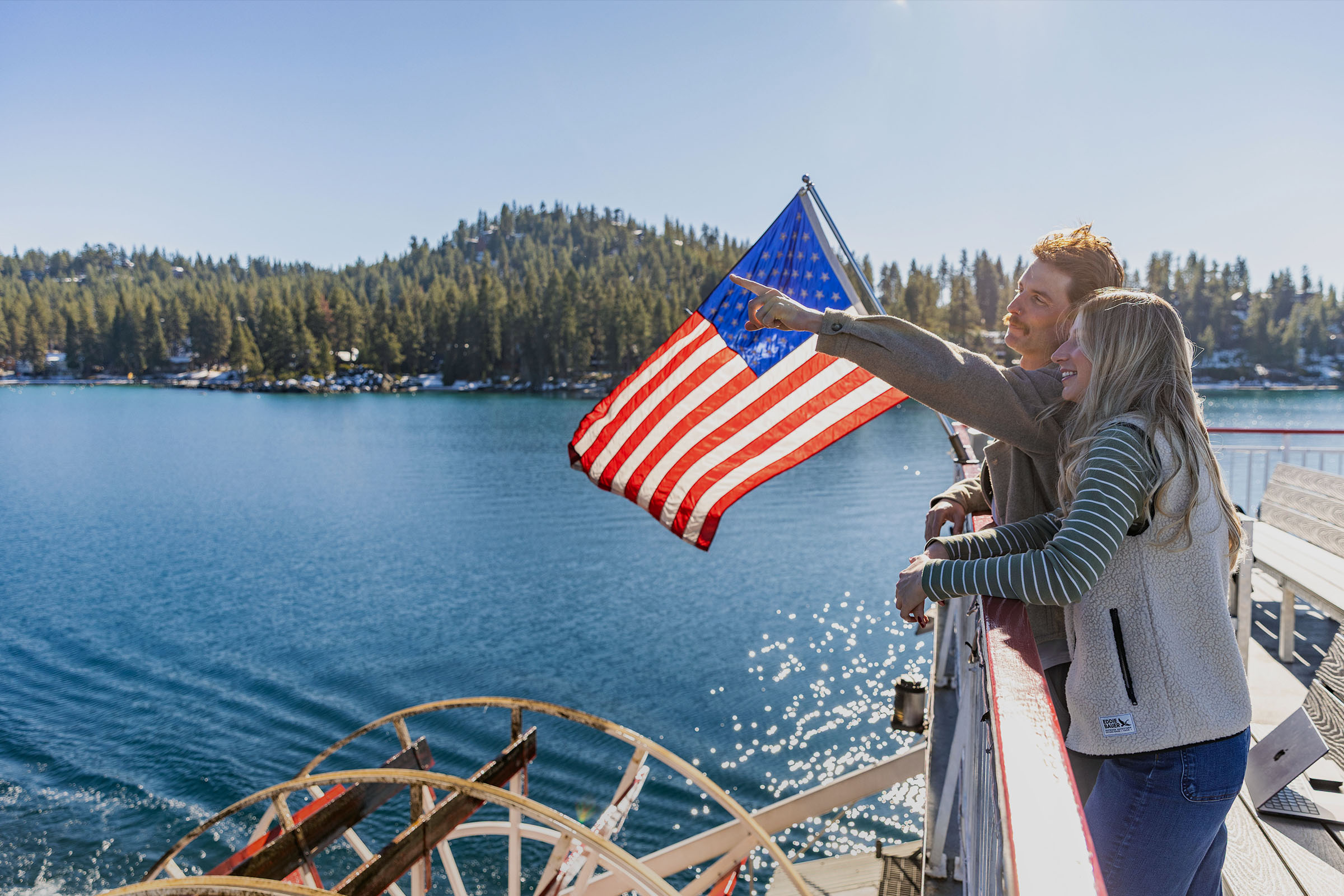 A couple enjoying a riverboat cruise with an American flag waving in the background.