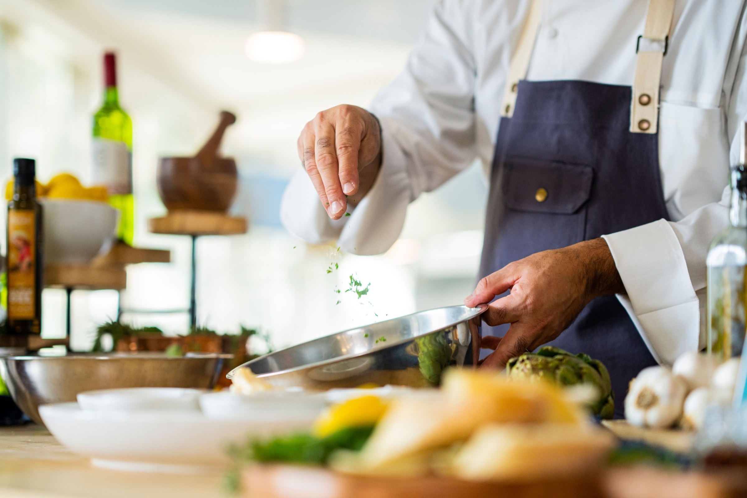 Chef sprinkling spices into a cooking bowl.