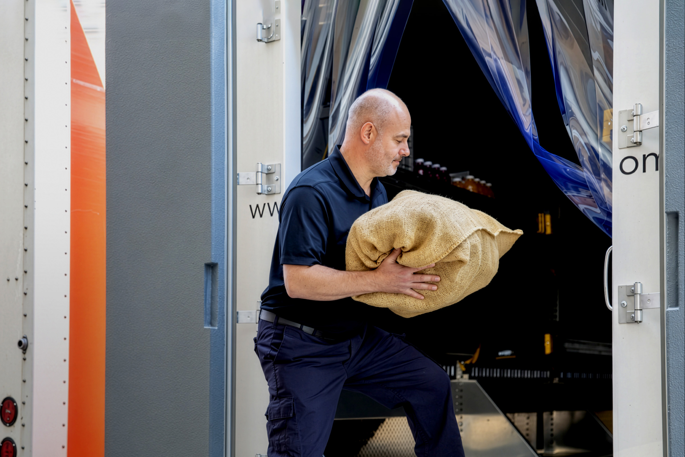 Employee putting a burlap sack into the back of a tractor-trailer.