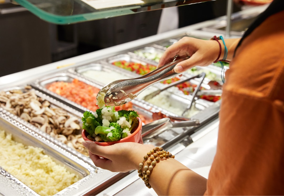 A student building their salad at a salad bar.