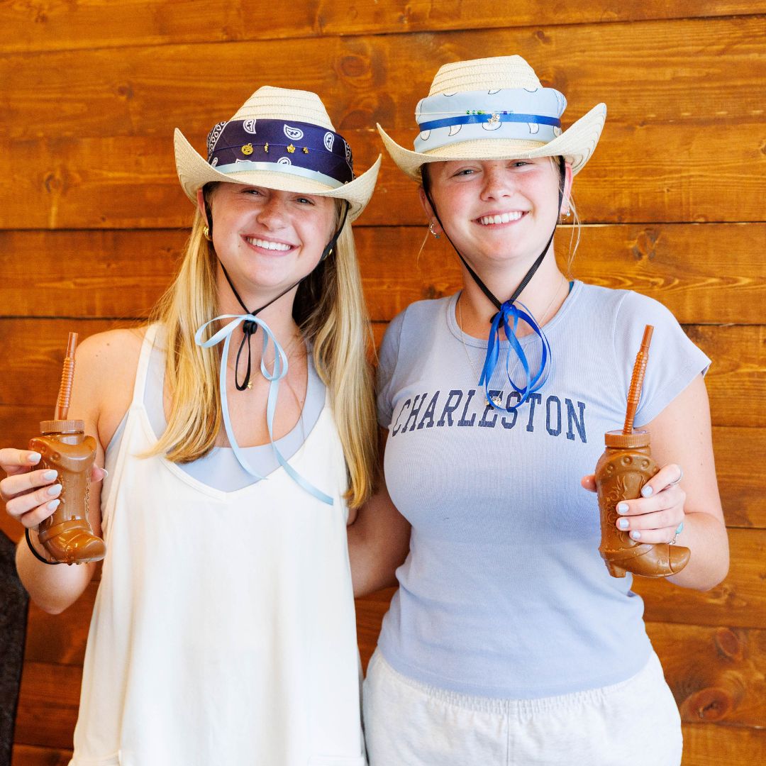two girls in cowboy hats drinking cowboy boot shaped drinks.
