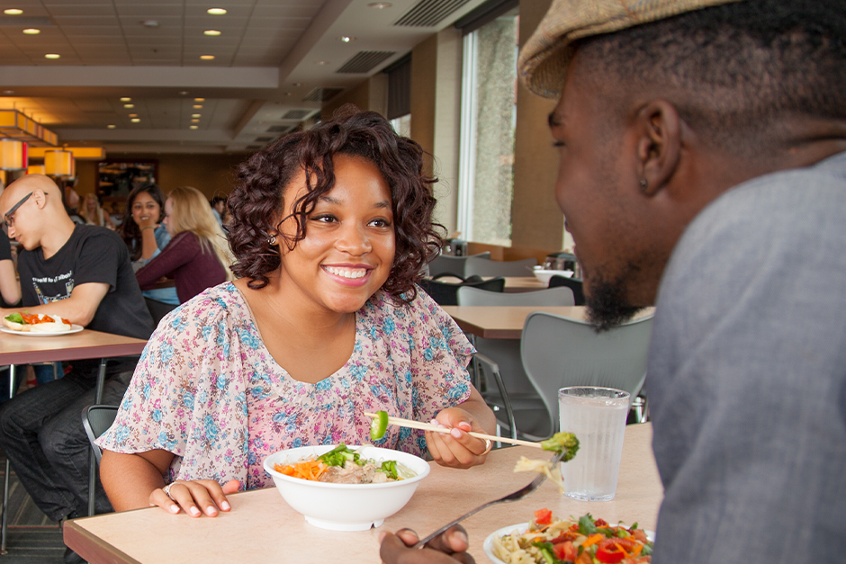 Two college students sitting and eating in a dining hall.
