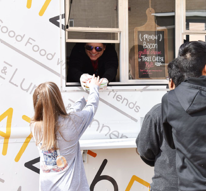 A smiling food truck employee handing food to a customer.